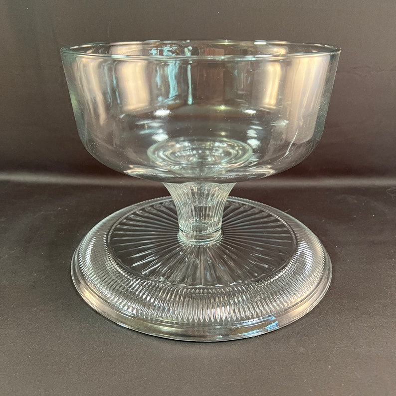 May include: A clear glass pedestal bowl with a fluted base. The bowl is designed for serving desserts or other foods.