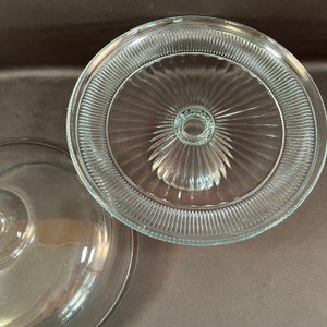 May include: A clear glass cake stand with a fluted edge and a pedestal base. The stand is designed for serving cakes and other desserts.