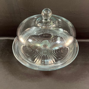 May include: A clear glass cake stand with a domed lid. The stand has a fluted edge and the lid has a knob on top.