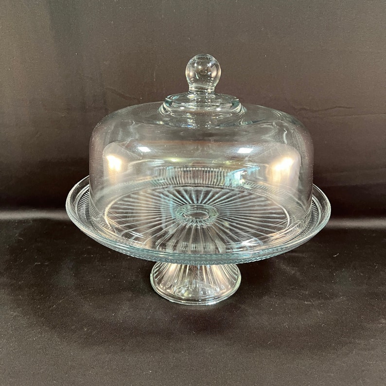 May include: A clear glass cake stand with a domed lid. The stand has a fluted base and a clear glass plate.