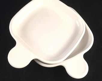 May include: Two white ceramic square baking dishes with handles. The dishes are stacked on top of each other.