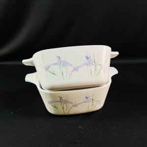 May include: Two white ceramic baking dishes with a floral design. The dishes feature a light blue and purple iris flower pattern on a white background.