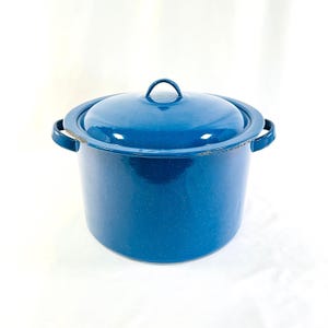 May include: A blue enamel pot with a matching lid. The pot has two side handles and a small handle on the lid. The pot has white speckles and a slightly distressed appearance, suggesting vintage use. The pot is on a white background.