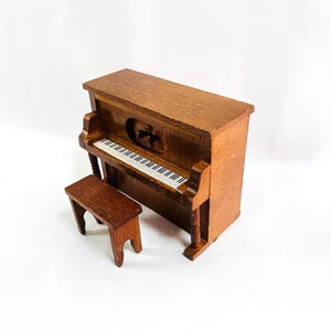 May include: A miniature wooden piano with a matching bench. The piano has a detailed keyboard with black and white keys. The wood has a warm, brown tone. The bench is small and simple, complementing the piano's design.