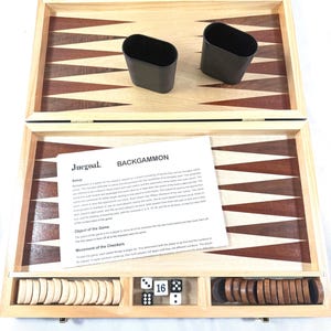 May include: Open backgammon board with a light wood frame and a dark wood playing surface. Includes black dice cups, white and brown game pieces, and dice. A sheet of paper with the title "BACKGAMMON" is visible.