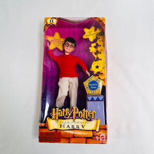 May include: A Harry Potter Wizard Sweets doll of Harry Potter in a red sweater and white pants. The doll is holding a yellow star with the text "Special Bracelet Just for you!" The doll is packaged in a box with a purple background and the text "Harry Potter Wizard Sweets™ Harry".