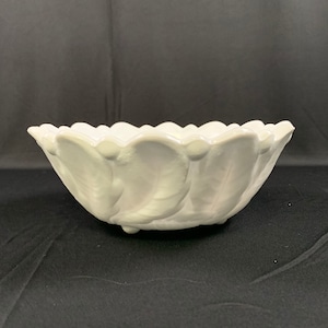 May include: White ceramic bowl with a scalloped rim and a leaf design. The bowl has three small feet.