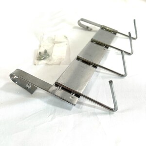 May include: A silver-colored metal coat rack with three hooks and a mounting bracket. The rack is designed to be mounted on a wall or door. A small bag of screws is also included.