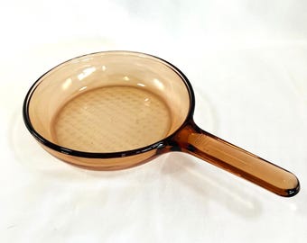May include: A brown glass frying pan with a textured bottom and a long handle.