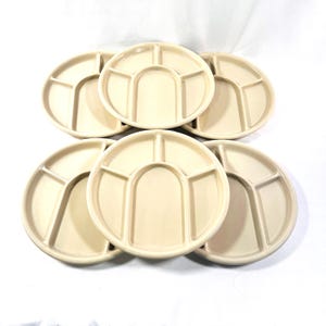 May include: Six off-white, divided serving plates. Each plate is round with four sections, including a large central compartment and three smaller ones. The plates are arranged on a white surface, offering a clean, neutral aesthetic.