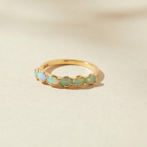 Può includere: Un anello con fascia in oro con sette opali di forma ovale incastonati in fila. Gli opali sono di colore verde pallido e bianco.
