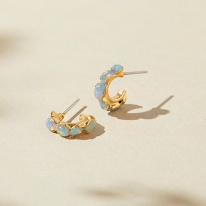 May include: A pair of gold hoop earrings with a row of iridescent opal stones. The earrings are small and delicate.
