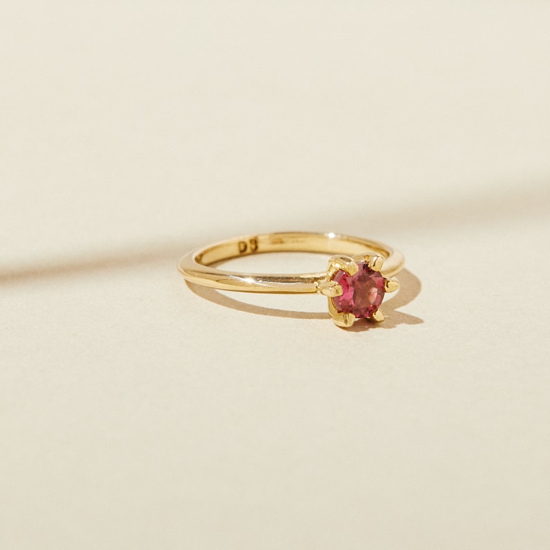 Puede incluir: Un anillo de oro con una sola piedra preciosa redonda de color rosa engastada en garras.