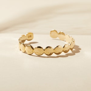 May include: A gold-toned hammered metal cuff bracelet with a rounded, scalloped design. The bracelet has a small inscription that reads "DB".