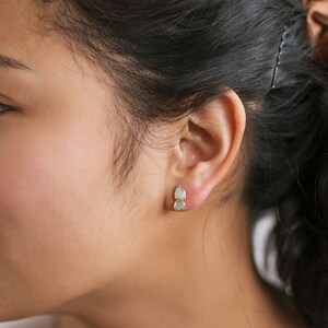 Raw opal and aquamarine studs worn on a model with dark hair. March and October birthstone earrings with natural texture.