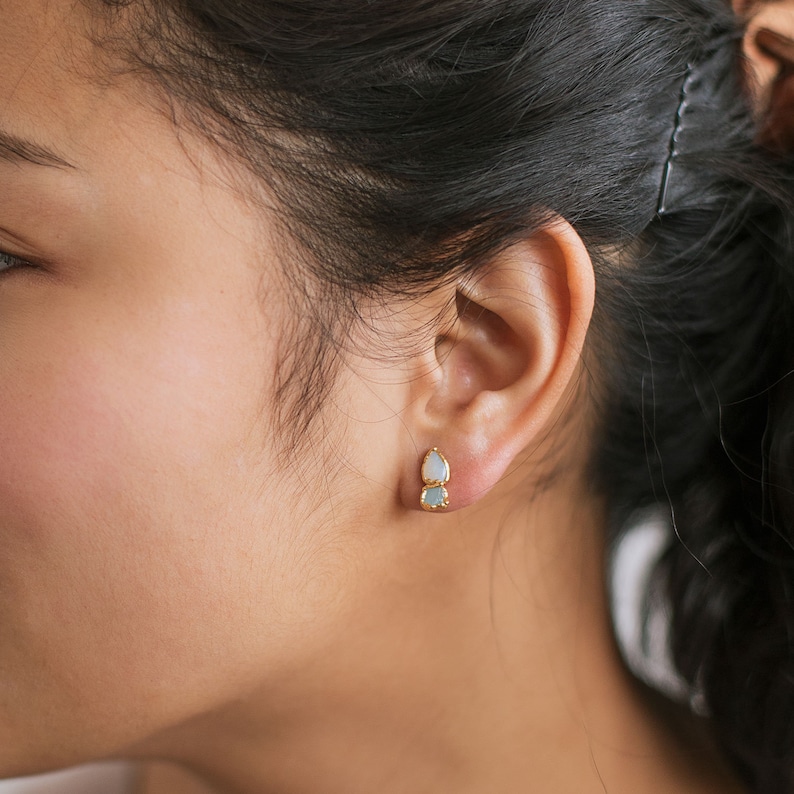 Raw opal and aquamarine studs worn on a model with dark hair. March and October birthstone earrings with natural texture.