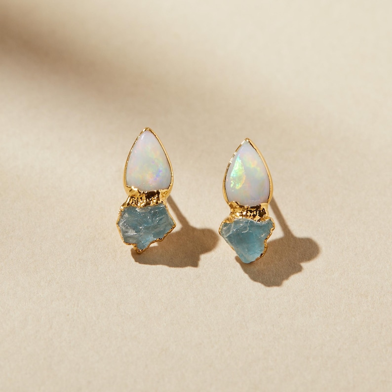Raw opal studs paired with rough aquamarine crystals on a neutral background. Handmade March and October birthstone earrings.