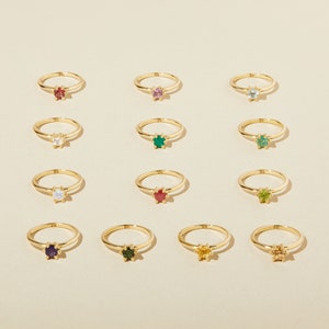 Puede incluir: Doce anillos de oro con piedras preciosas de diferentes colores. Los anillos est&aacute;n dispuestos en cuatro filas de tres. Las piedras preciosas son rojo, rosa, azul, blanco, verde, peridoto, rub&iacute;, amatista, esmeralda, citrino y topacio.