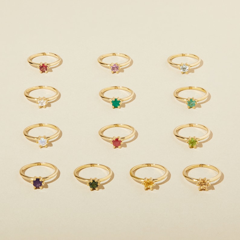 Puede incluir: Doce anillos de oro con piedras preciosas de diferentes colores. Los anillos est&aacute;n dispuestos en cuatro filas de tres. Las piedras preciosas son rojo, rosa, azul, blanco, verde, peridoto, rub&iacute;, amatista, esmeralda, citrino y topacio.