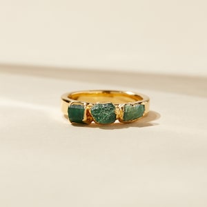 May include: A gold ring with three green gemstones set in the band.