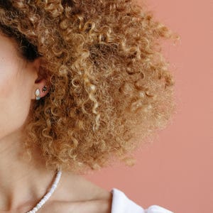 Raw aquamarine and opal studs worn on a model with curly hair. Organic crystal earrings for everyday wear.