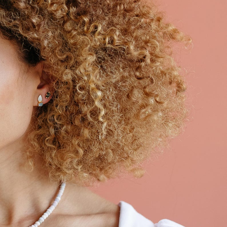 Raw aquamarine and opal studs worn on a model with curly hair. Organic crystal earrings for everyday wear.