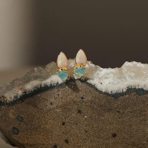 Rough opal and aquamarine earrings styled on textured stone. Natural handmade gemstone studs.