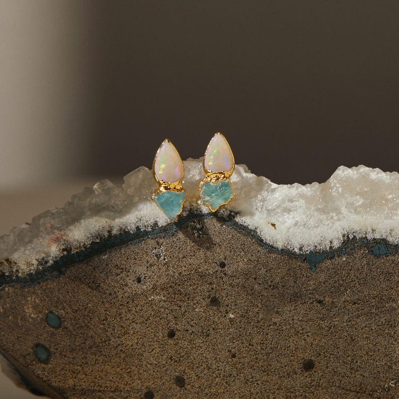 Rough opal and aquamarine earrings styled on textured stone. Natural handmade gemstone studs.