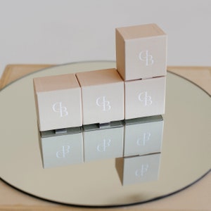 May include: Six small, square, light brown boxes with the letters "CB" printed in white on each box. The boxes are arranged in a pyramid shape on a silver tray.