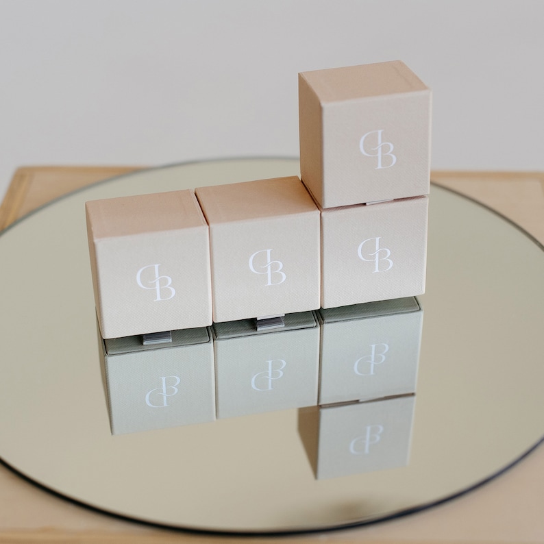 May include: Six small, square, light brown boxes with the letters "CB" printed in white on each box. The boxes are arranged in a pyramid shape on a silver tray.