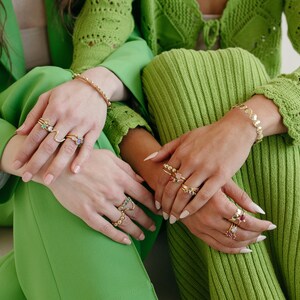 Puede incluir: Dos personas con ropa verde con anillos de oro en los dedos. Los anillos est&aacute;n decorados con piedras preciosas de colores.