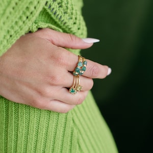 May include: A hand wearing three gold rings with green gemstones. The rings are stacked on the finger.