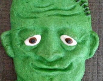Puede incluir: Galletas de jengibre verdes con forma de cara de Frankenstein con glaseado marrón y costuras negras.