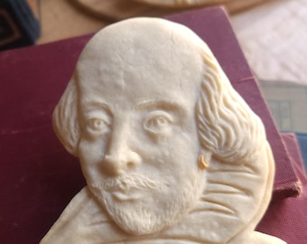 May include: A white sugar cookie shaped like a bust of William Shakespeare. The cookie has a detailed design of Shakespeare's face, hair, and collar.