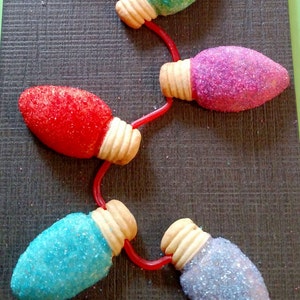 Op de afbeelding: Een string van lampvormige koekjes versierd met kleurrijke sprinkles. De koekjes zijn verbonden met rood touw.