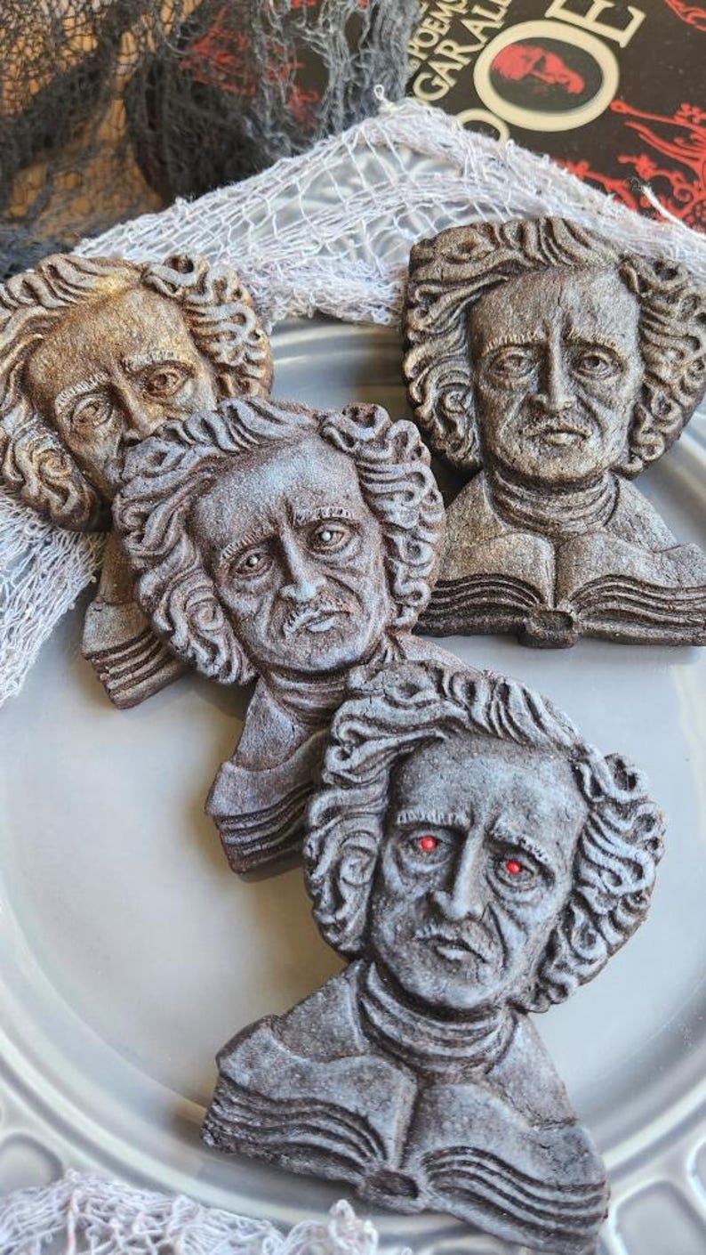 Puede incluir: Una colecci&oacute;n de decoraciones con forma de busto de Edgar Allan Poe. Los bustos son en tonos grises y marrones, con rasgos faciales detallados y cabello rizado. Un busto tiene ojos rojos brillantes. Los bustos est&aacute;n dispuestos sobre un plato gris.