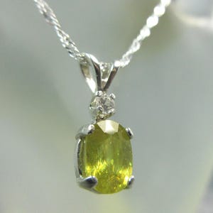 May include: A silver pendant necklace featuring a light green oval gemstone. The gemstone is set in a silver bezel and is topped with a small, round, clear stone. The necklace chain is a delicate silver cable.