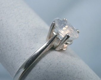 May include: A silver ring featuring a pear-shaped, iridescent gemstone. The ring's band is smooth and polished, with the gemstone held in place by four prongs. The gemstone has a subtle, multi-colored shimmer.