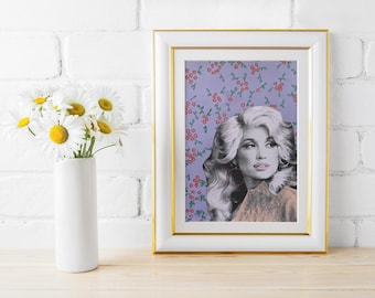 Può includere: Una stampa incorniciata con un'immagine in bianco e nero di una donna con i capelli biondi, su uno sfondo lavanda con un motivo floreale. La cornice è bianca con un bordo dorato. Un vaso bianco con margherite è su una superficie di legno.