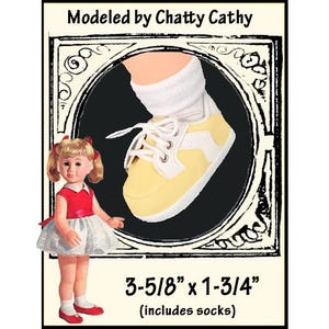 May include: A yellow and white lace-up sneaker with a white sole and white laces, worn with a white sock. The image includes the text Modeled by Chatty Cathy and dimensions of 3-5/8 inches by 1-3/4 inches, which includes the socks for the doll.
