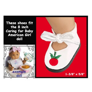 May include: White doll shoes with a red embroidered tomato design. The shoes are 1-3/8 inches by 5/8 inches and fit the 8 inch Caring for Baby American Girl doll.