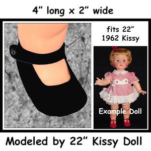 May include: Black doll shoes, 4 inches long and 2 inches wide, with a buttoned strap. The shoes are modeled by a 22-inch 1962 Kissy doll. The image includes the text "Example Doll".