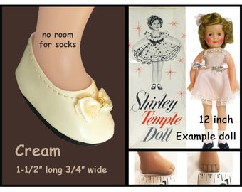 May include: Cream-colored doll shoes with a bow on the toe. The shoes are 1 1/2 inches long and 3/4 inches wide. The shoes are modeled by a 12 inch Shirley Temple doll. The image also includes a box for the doll, which says "Shirley Temple Doll" and "12 inch Example doll".