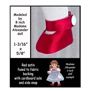 May include: A close-up of a red satin doll shoe with a white button closure. The shoe is fused to fabric backing with a cardboard sole and side snap. The shoe is modeled by an 8-inch Madame Alexander doll. The shoe measures 1-3/16" x 5/8".