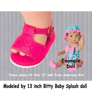 May include: Bright pink doll sandals with a buckle closure. A doll wearing a blue and teal swimsuit and matching sun hat is also shown. The text "Example Doll" is printed on the doll. The text "These shoes fit this 13" doll from American Girl" is also shown.