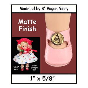 May include: A close-up of a pink doll shoe with a gold button. The shoe is 1 inch by 5/8 inch. The image also shows a doll wearing the shoe. The text in the image says "Modeled by 8" Vogue Ginny", "Matte Finish", "Ginny Example Doll", and "wearing rayon socks".