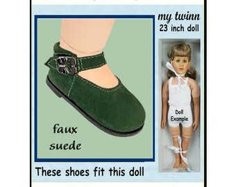 May include: A dark green faux suede doll shoe with a butterfly-shaped buckle strap. The text reads: Modeled by 23" My Twinn Doll, my twinn 23 inch doll, Doll Example, faux suede, These shoes fit this doll, and the dimensions 3-7/8" x 1-5/8".