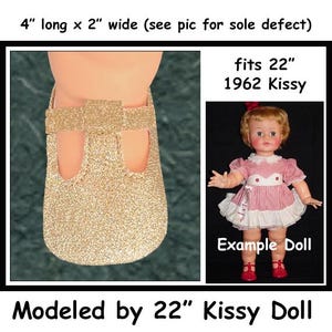 May include: Gold glitter doll shoes, 4 inches long and 2 inches wide, designed to fit a 22-inch 1962 Kissy doll. The shoes have a Mary Jane style with two cut-out openings. The image includes an example doll.