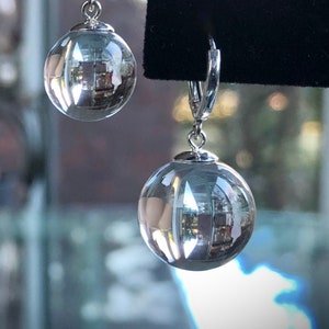 May include: A pair of silver hoop earrings with clear glass ball charms. The glass balls reflect the surrounding environment.
