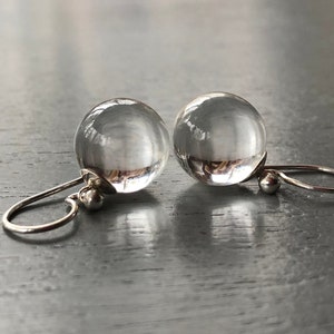 May include: A pair of silver earrings with clear glass ball pendants. The earrings have a simple design and are perfect for everyday wear.